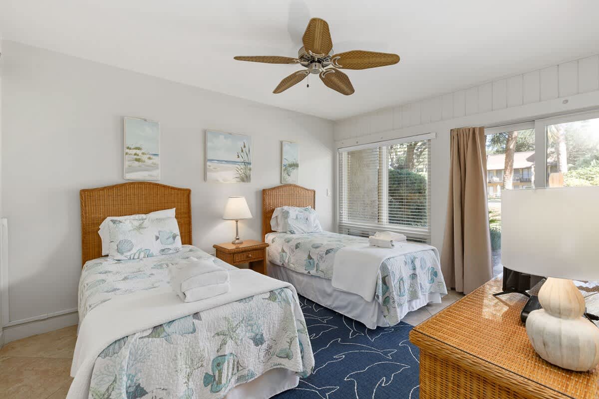 Relax in this coastal twin bedroom with wicker furniture, ocean-inspired bedding, and a cooling ceiling fan for your comfort.