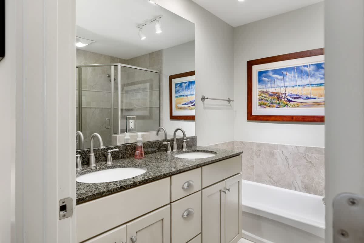 Unwind in your elegant bathroom featuring dual sinks, granite countertops, and a relaxing tub-shower combo with coastal artwork.