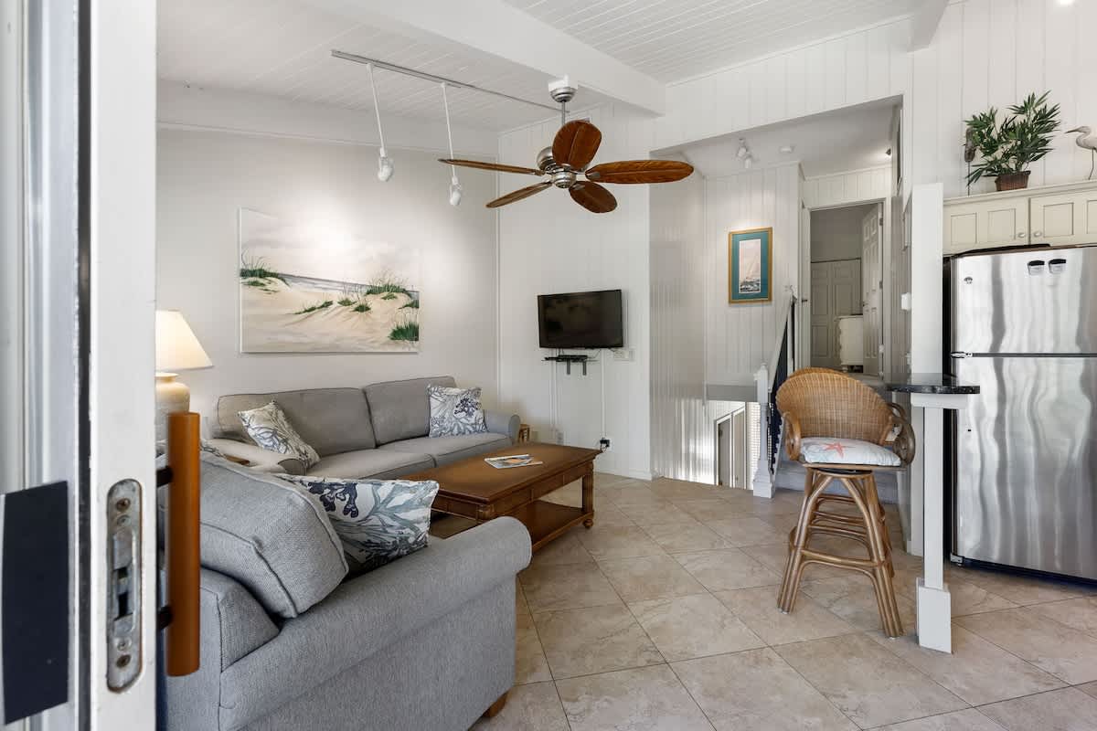 Sink into the cozy sectional and enjoy your coastal retreat with ocean-themed art, tropical ceiling fan, and modern kitchen nearby.