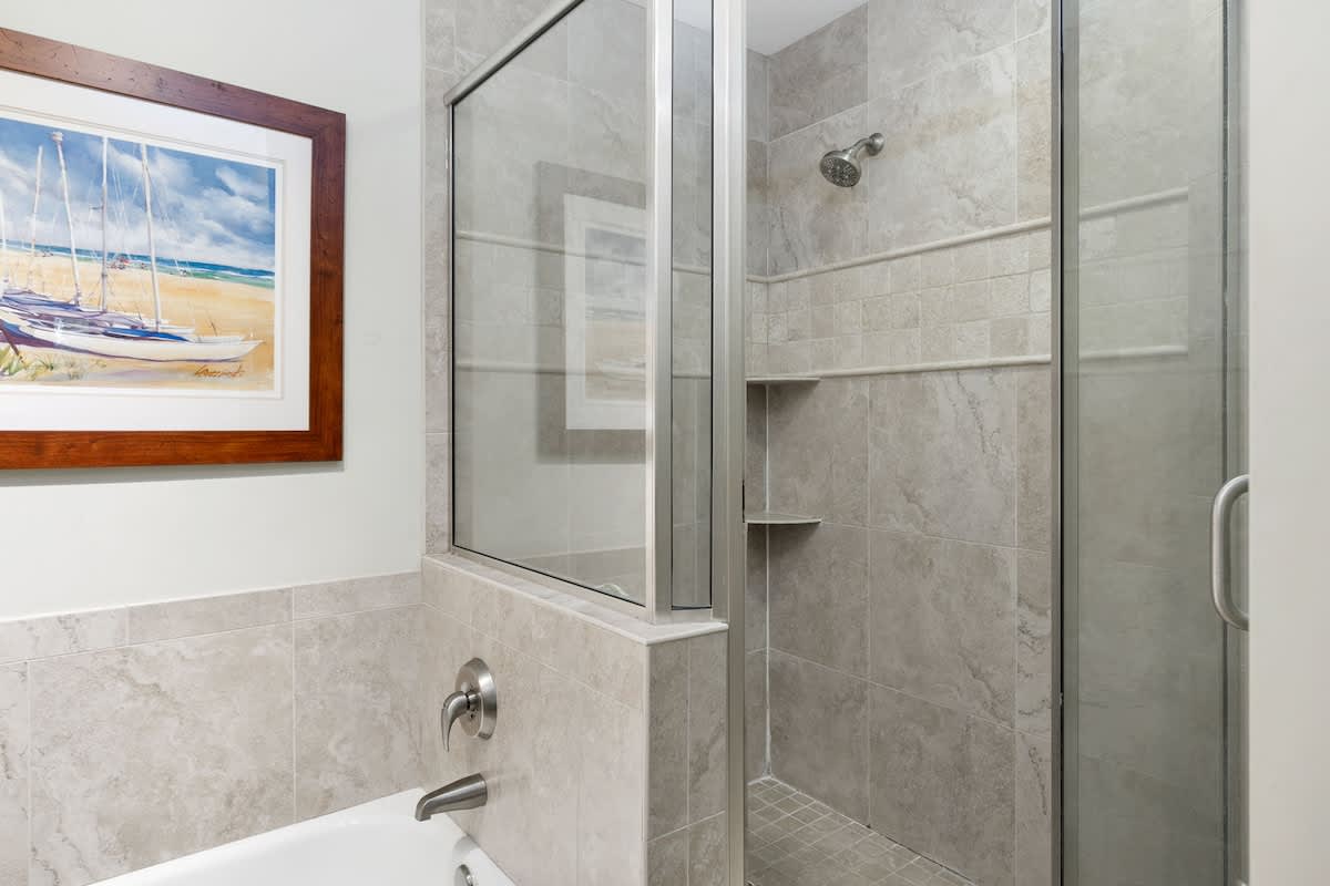 Refresh in your elegant marble bathroom with a spacious glass shower and beautiful beach artwork to inspire your coastal getaway dreams.