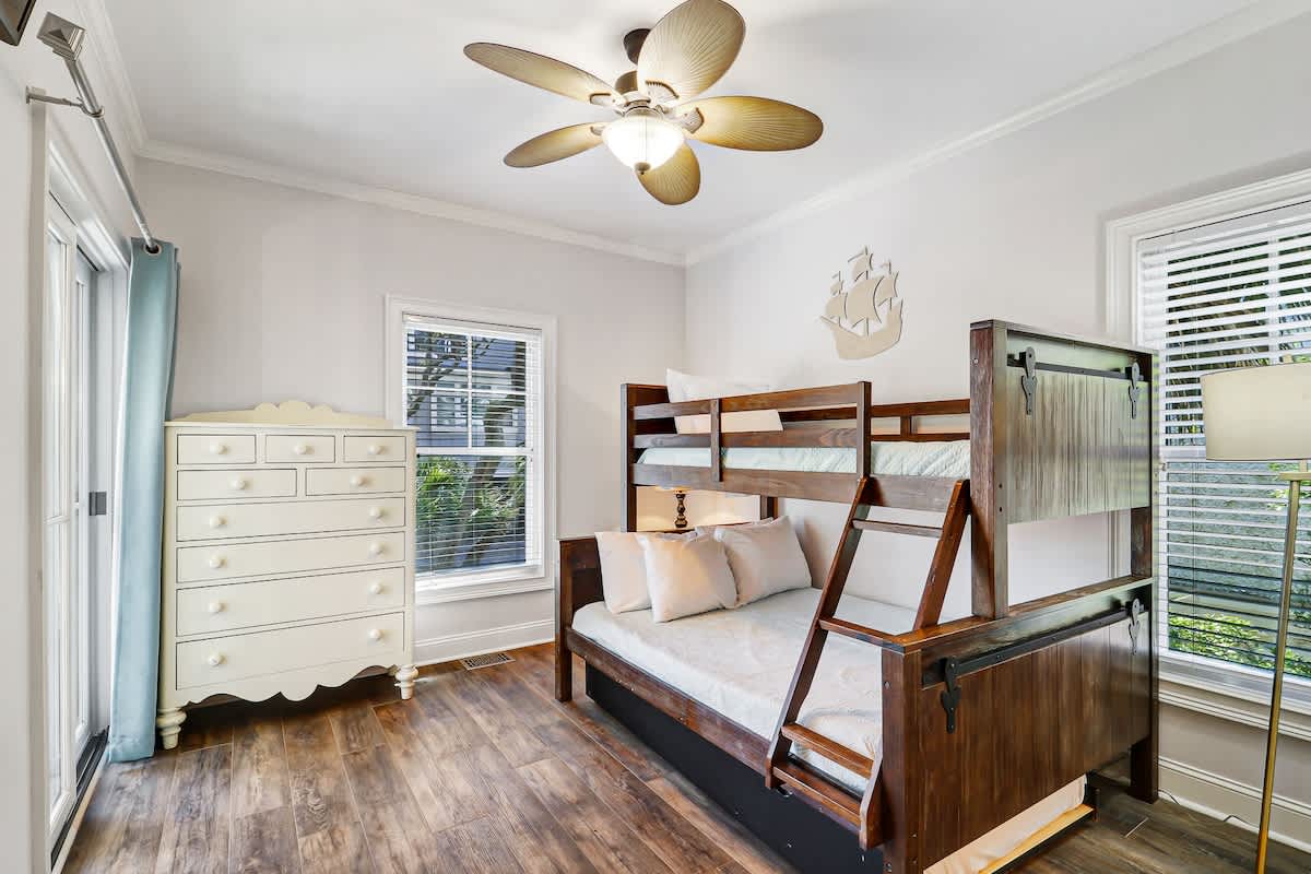 Spacious bedroom with a twin-over-full bunk bed, hardwood floors, dresser storage, and a large window that fills the room with natural light.