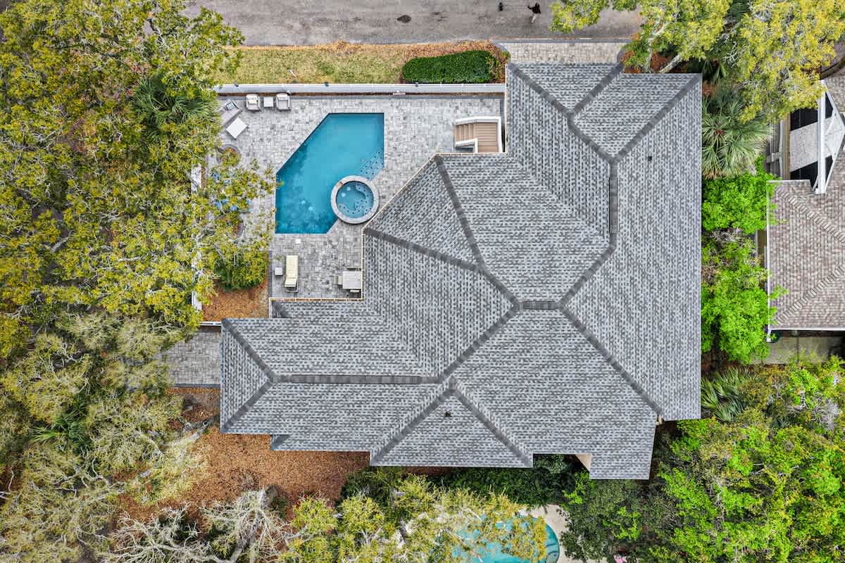 Aerial view of vacation rental property featuring swimming pool, hot tub, and spacious tile roof surrounded by lush tropical landscaping.