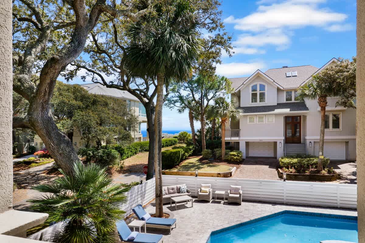 Elegant coastal home with private pool surrounded by tropical palms and mature oak trees, offering a peaceful retreat near the ocean.