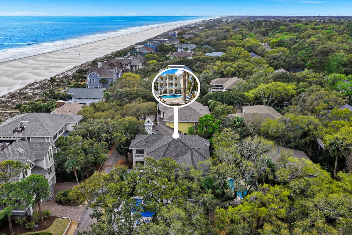 Aerial view of beachfront property location nestled among lush trees, just steps from pristine sandy beach and crystal-clear waters.
