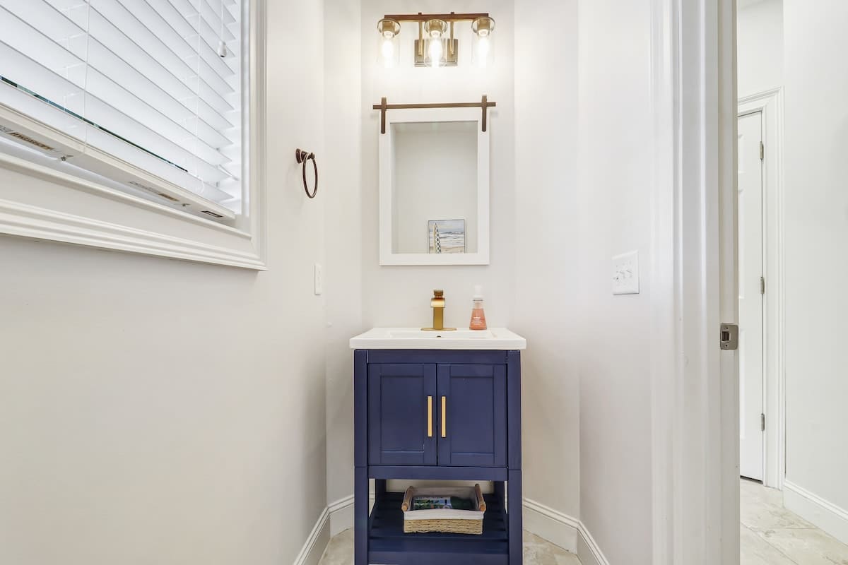 Refresh in your stylish powder room with navy vanity, brass fixtures, and natural light streaming through plantation shutters.
