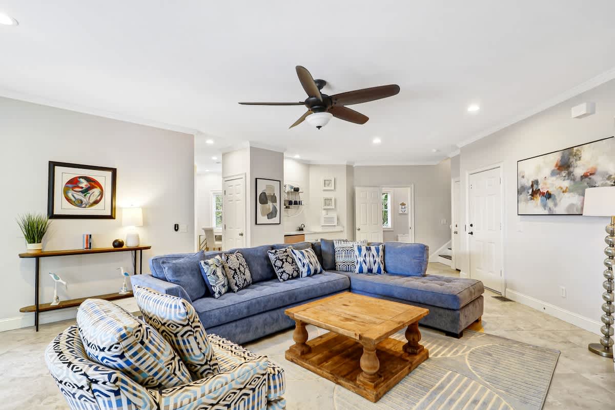Relax in your spacious living room featuring a plush blue sectional sofa, stylish decor, and modern ceiling fan for comfort.