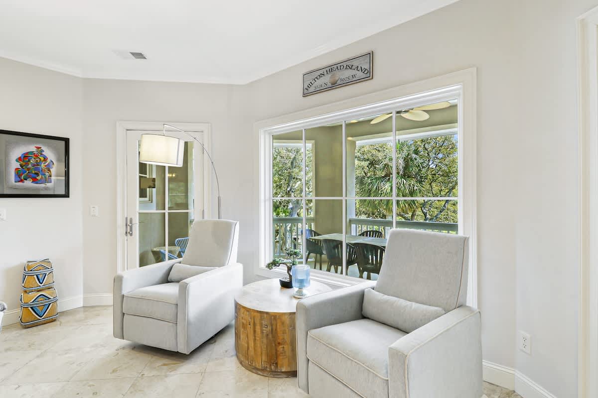 Unwind in your bright living room with plush seating, where floor-to-ceiling windows frame lush greenery for peaceful moments.