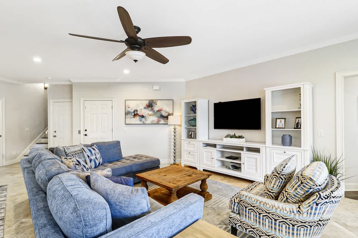 Unwind in your spacious living room with plush blue sectional seating, entertainment center, and ceiling fan for perfect comfort.