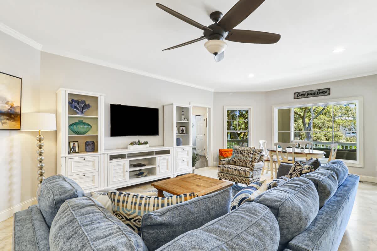 Relax in your bright, airy living room with plush seating, entertainment center, and peaceful garden views through oversized windows.