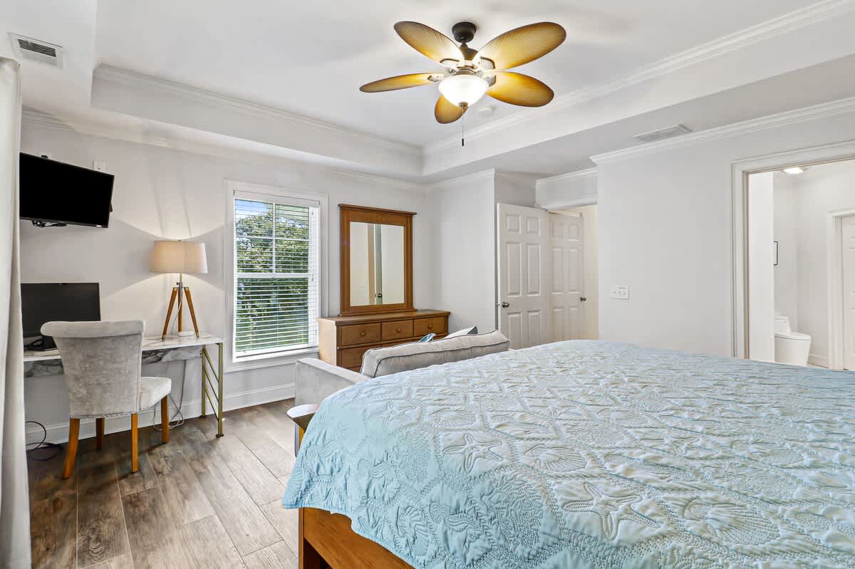 Rest easy in your peaceful bedroom with a cozy workspace, elegant ceiling fan, and calming natural light.