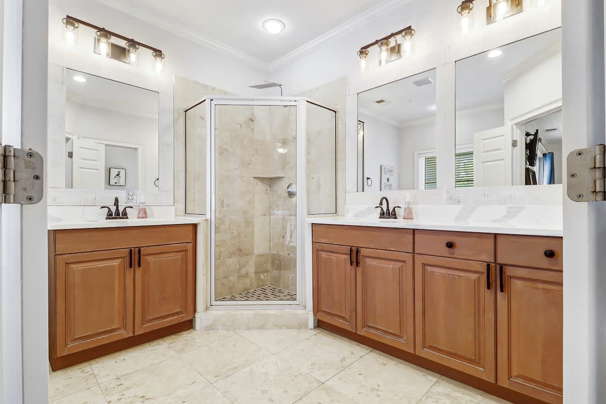 Step into your luxurious bathroom featuring dual vanities with warm wood cabinetry and a spacious glass-enclosed shower.