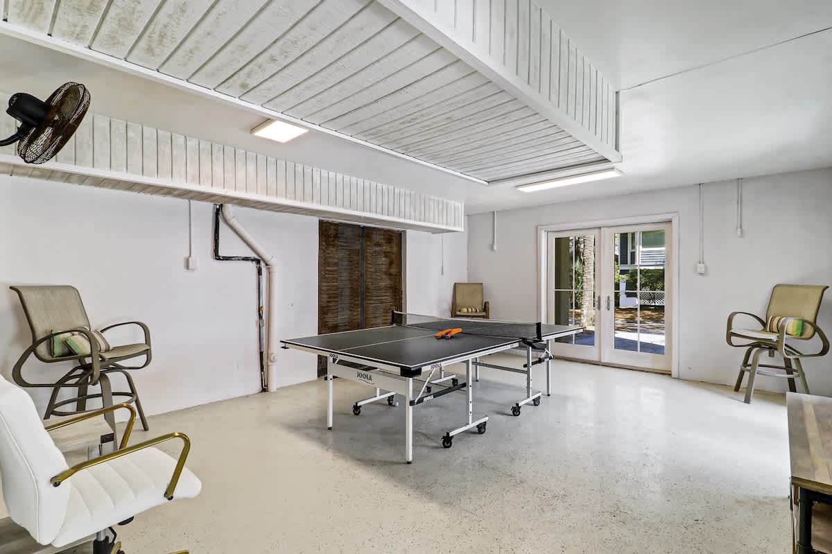 Your private game room awaits with ping pong fun under soaring white beams and tropical views through glass doors.