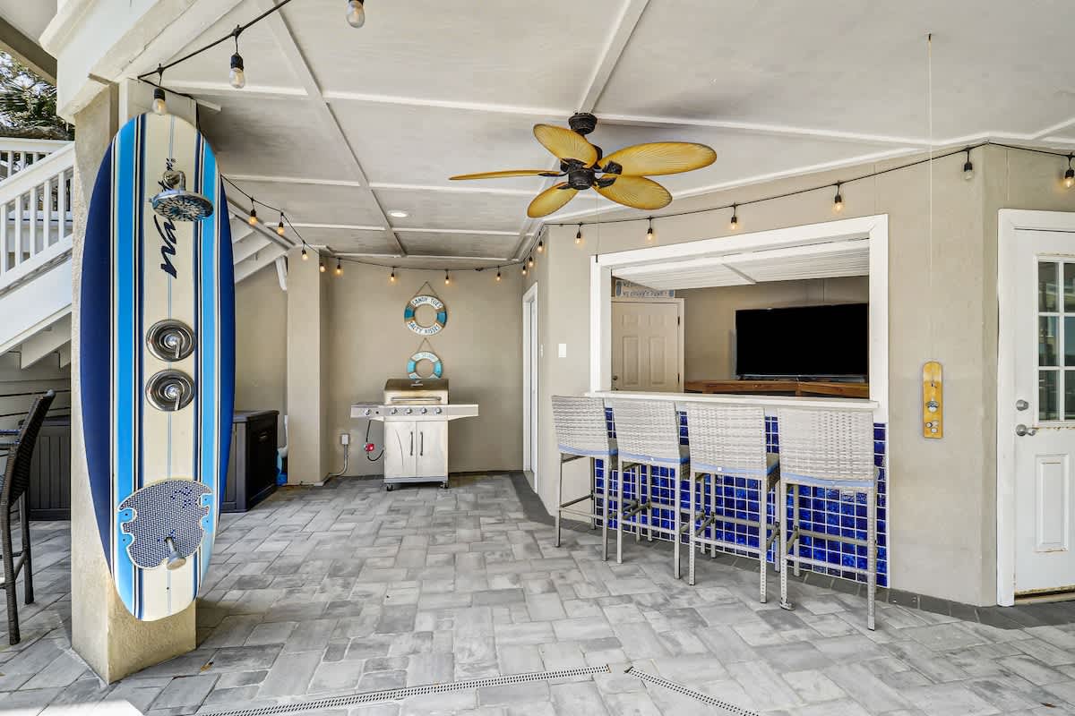 Your perfect beach-themed outdoor kitchen awaits with a full grill, bar seating, and coastal decor under twinkling string lights.