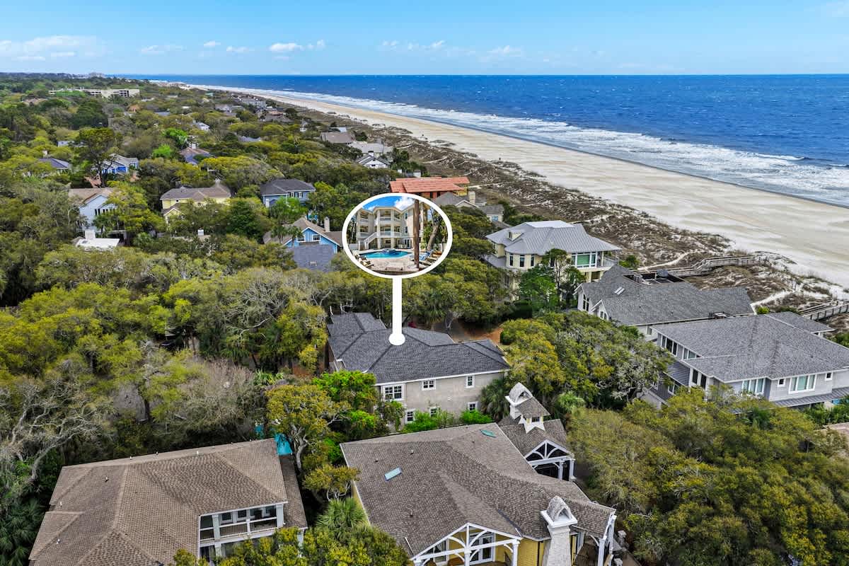 Stunning aerial view showcases the property's prime beachfront location, nestled among lush coastal trees just steps from pristine sandy shores and rolling ocean waves.