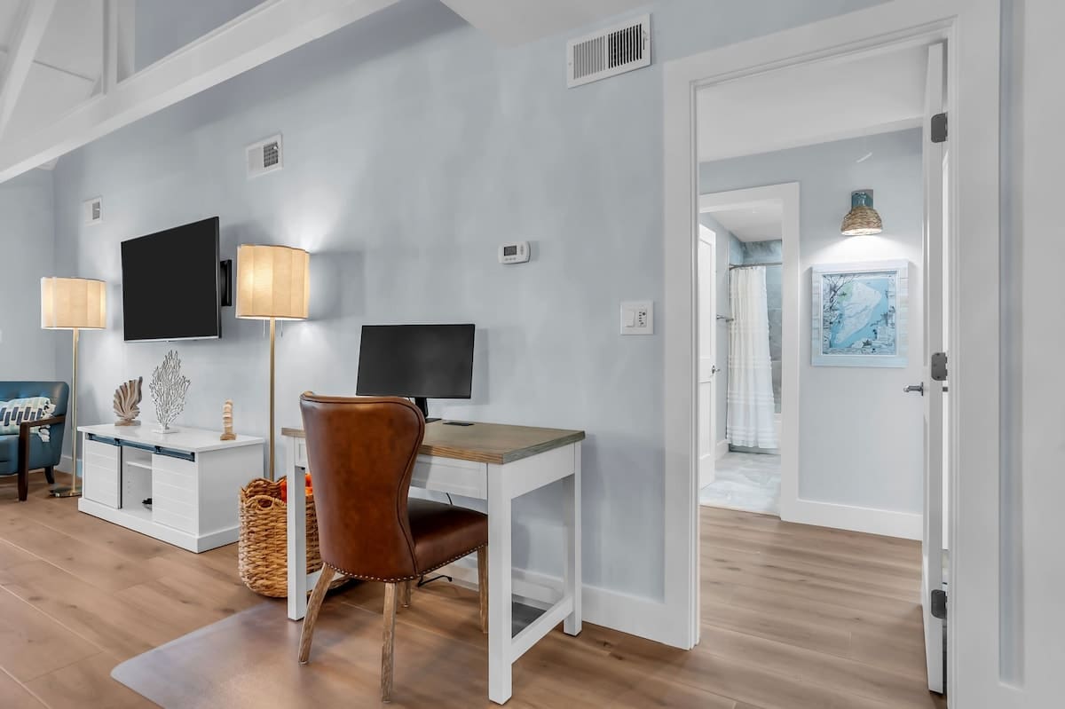 A thoughtfully designed workspace tucked into the living area, featuring a sleek desk, leather chair, and soft coastal hues that create a calm and productive atmosphere.