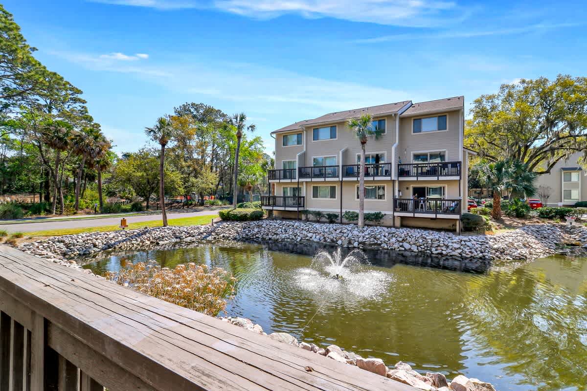 Multi-story residential building surrounded by lush landscaping and decorative pond with fountain feature.