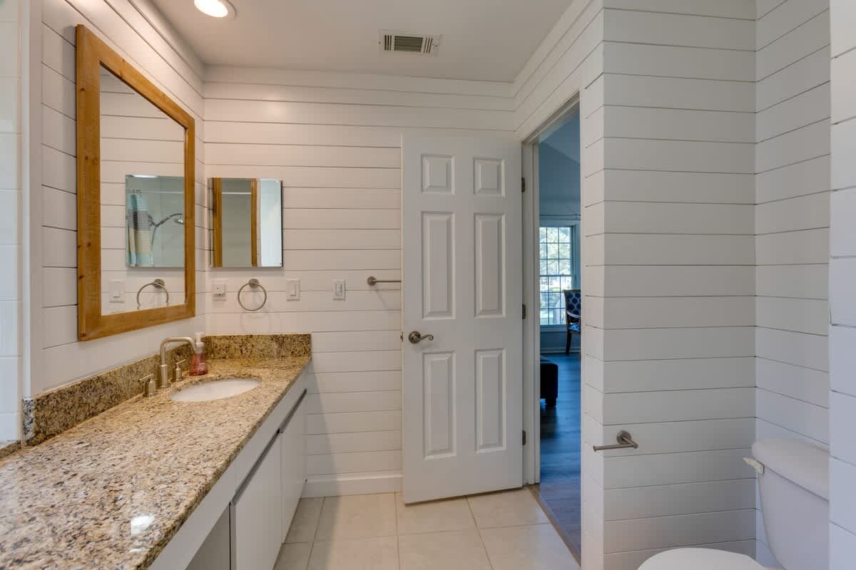 Step into your stylish bathroom featuring shiplap walls, granite countertops, and warm wood-framed mirrors that create a perfect coastal-modern retreat.