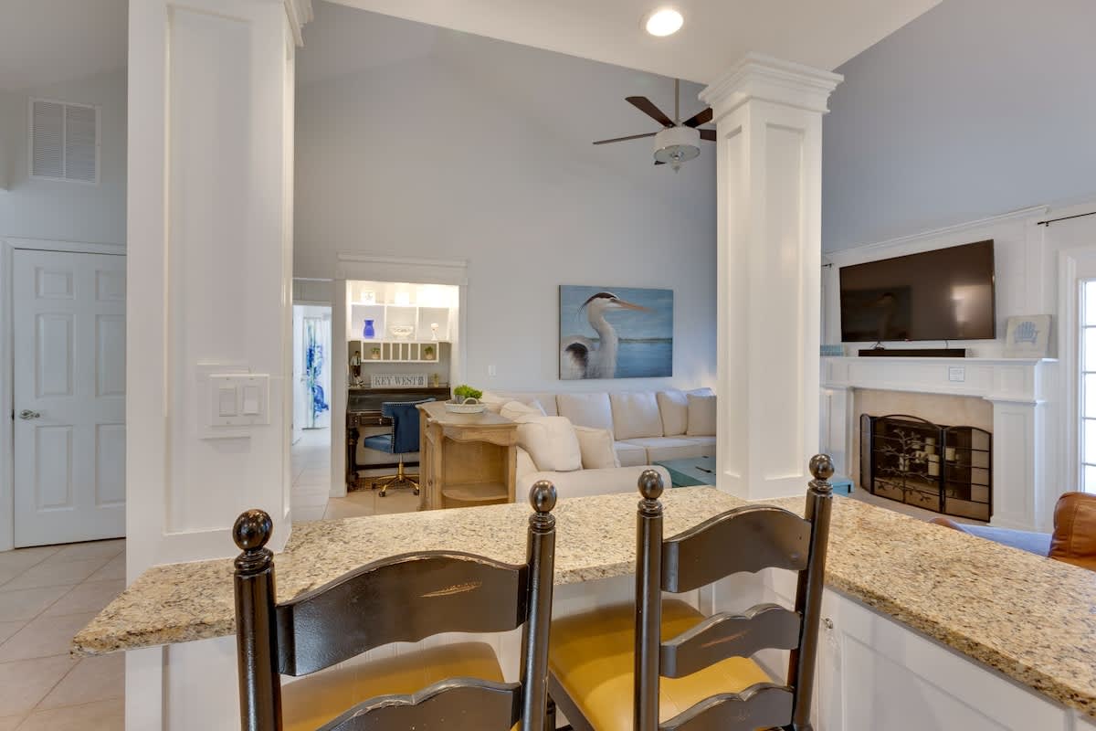 Relax in your spacious living area featuring soaring ceilings, coastal artwork, and a cozy fireplace—perfect for unwinding after beach days.