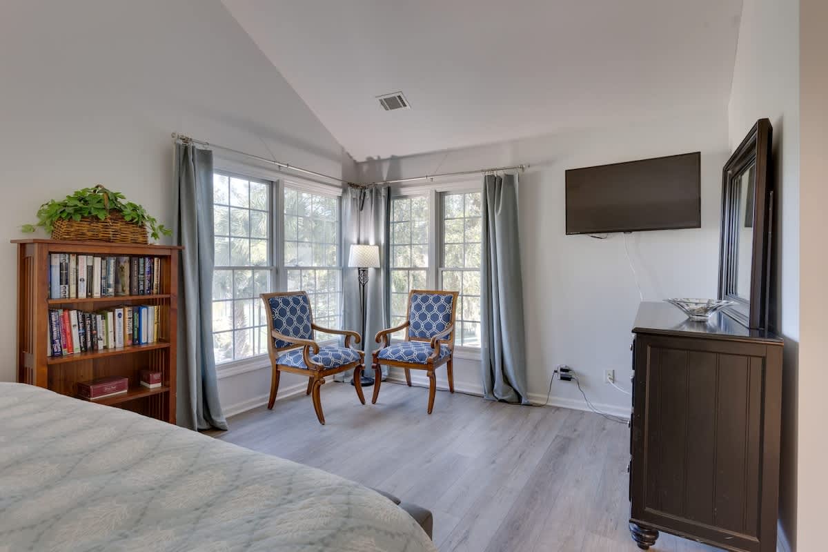 Relax in your bright bedroom featuring elegant seating by large windows, a cozy reading nook, and peaceful treetop views.