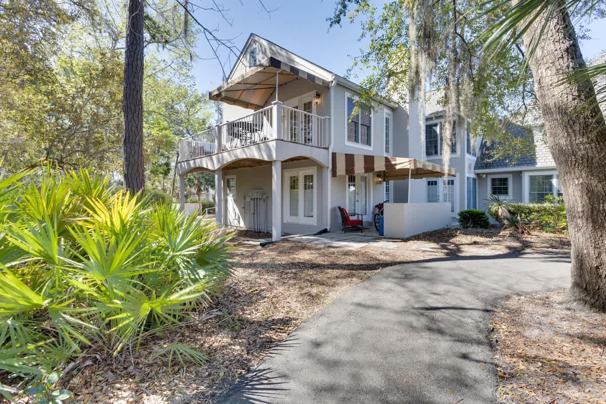 Charming white property nestled among mature trees and tropical landscaping, featuring balconies and welcoming entrance areas.