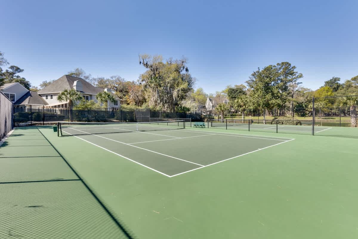 Professional tennis courts nestled in a peaceful residential setting with mature trees and blue skies overhead.