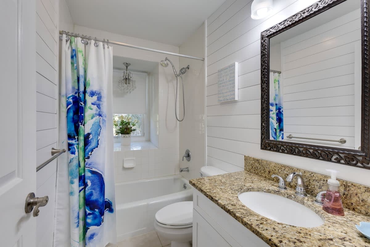 Refresh in your bright bathroom with granite counters, decorative mirror, and tub-shower combo featuring colorful curtains and coastal charm.