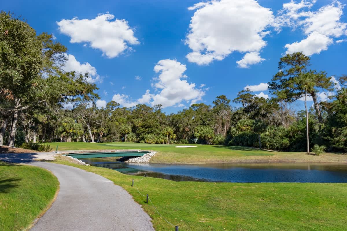 Beautiful golf course surroundings with manicured greens, water features, and scenic walking paths under clear blue skies.