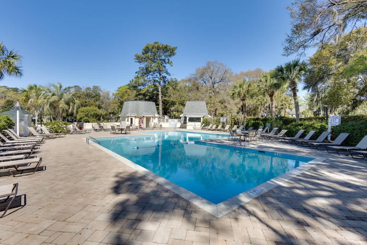 Beautiful community swimming pool surrounded by palm trees and tropical landscaping with comfortable lounge chairs.