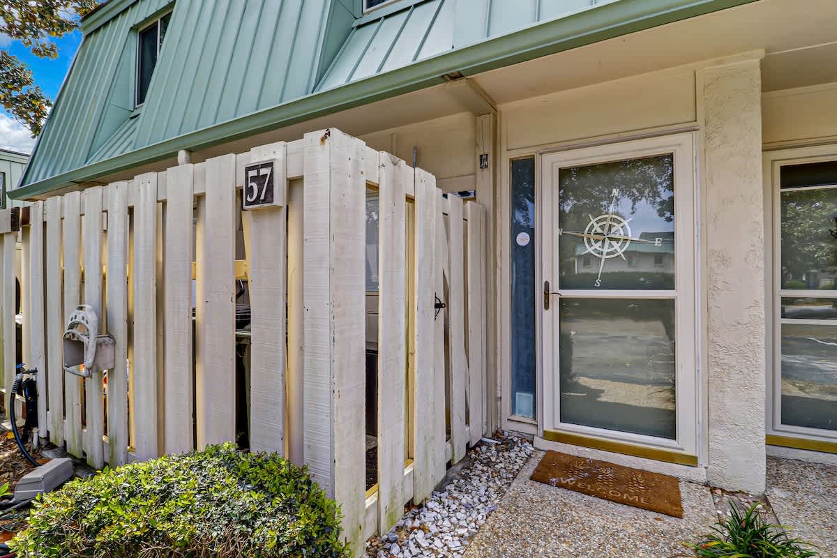 Charming property entrance with nautical compass window detail and private fenced courtyard area featuring natural landscaping.