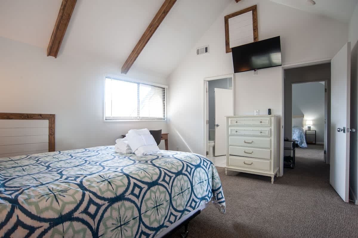 Relax in your peaceful bedroom sanctuary with vaulted ceilings, warm wood beams, and a cozy bed draped in beautiful blue linens.