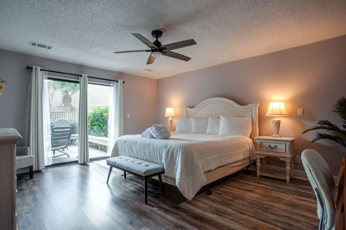 Sink into crisp white linens and enjoy the gentle breeze from your ceiling fan as natural light fills this serene bedroom.