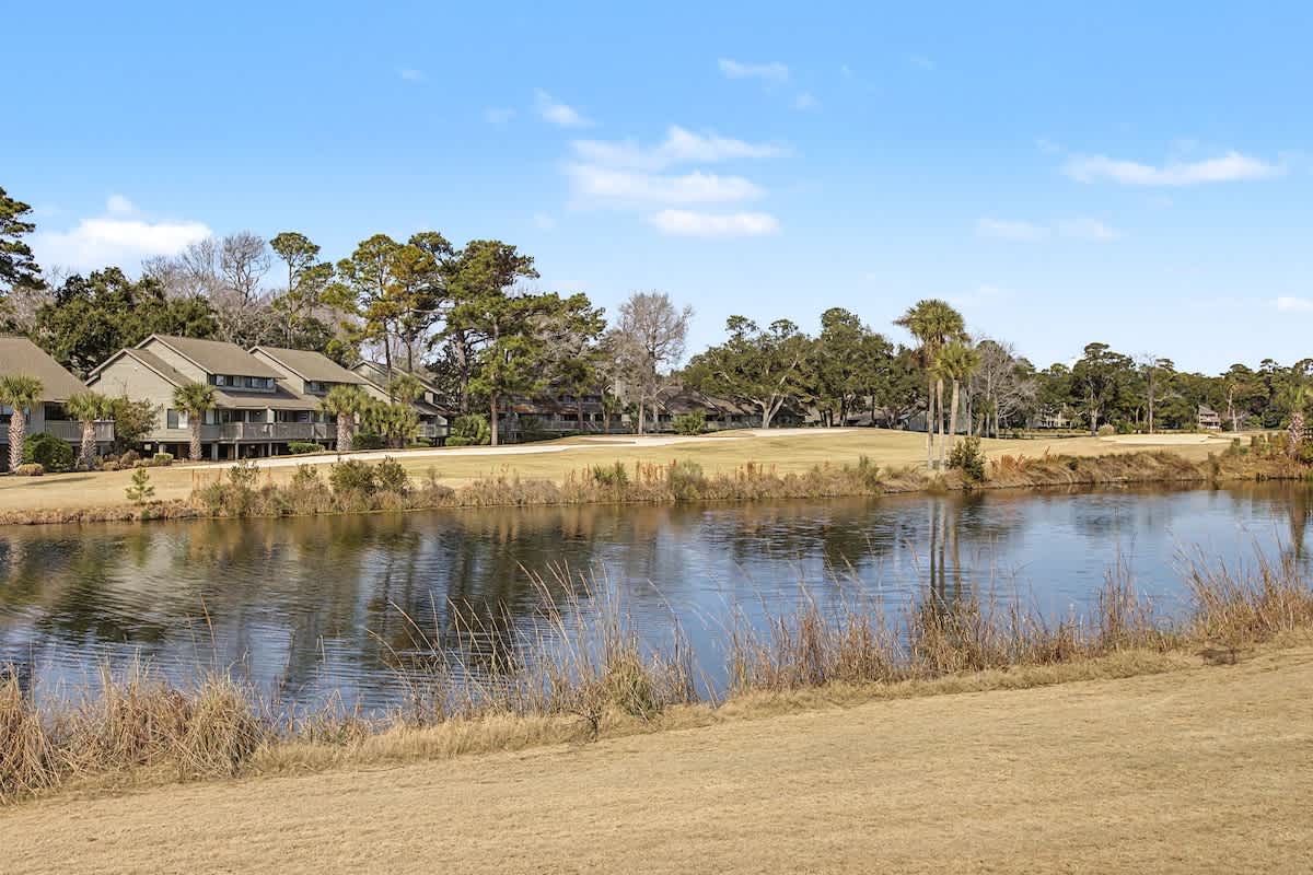 Golf course community featuring pristine fairways alongside a tranquil water hazard, surrounded by mature trees and residential properties.