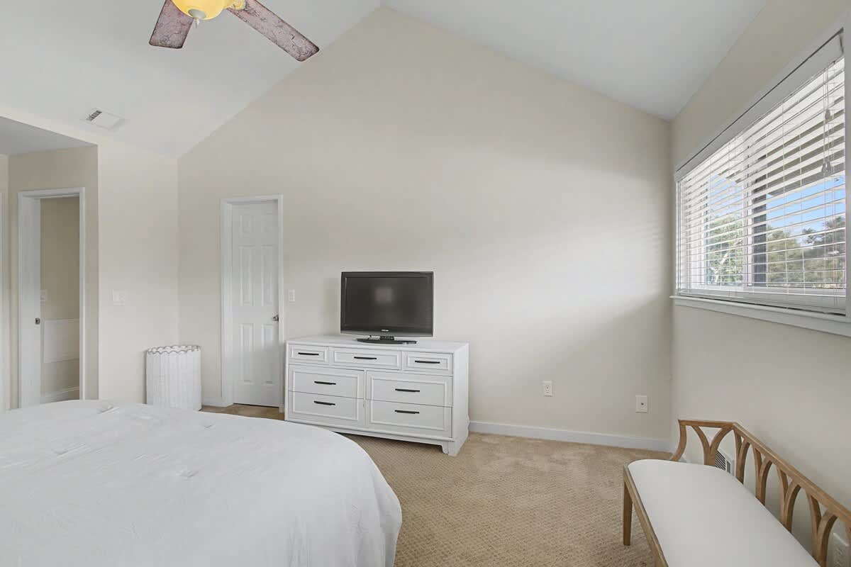 Rest peacefully in your serene bedroom featuring plush bedding, entertainment setup, and gentle natural light filtering through window blinds.