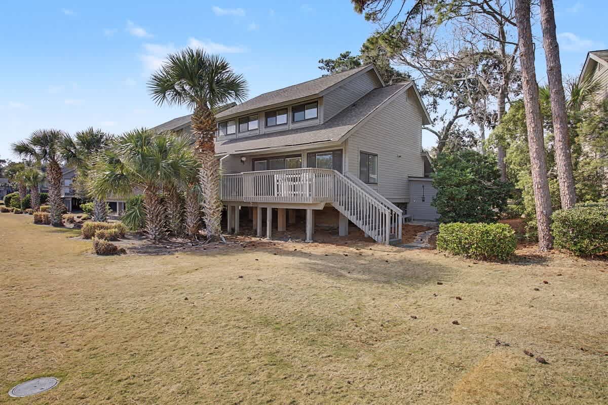 A charming coastal home nestled among tall pines and palm trees, featuring a spacious deck and natural landscaping in a peaceful residential setting.