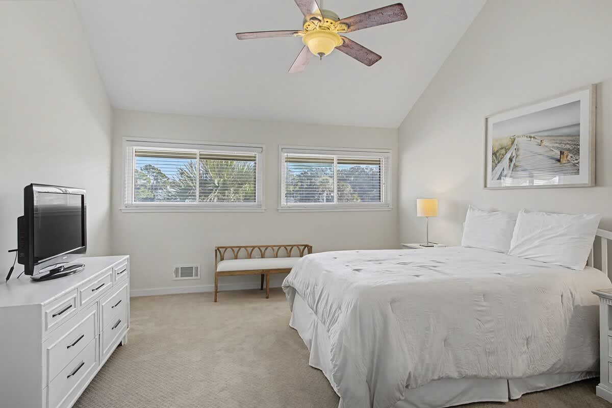 Rest in your serene bedroom with crisp white linens, gentle ceiling fan, and peaceful garden views through large windows.