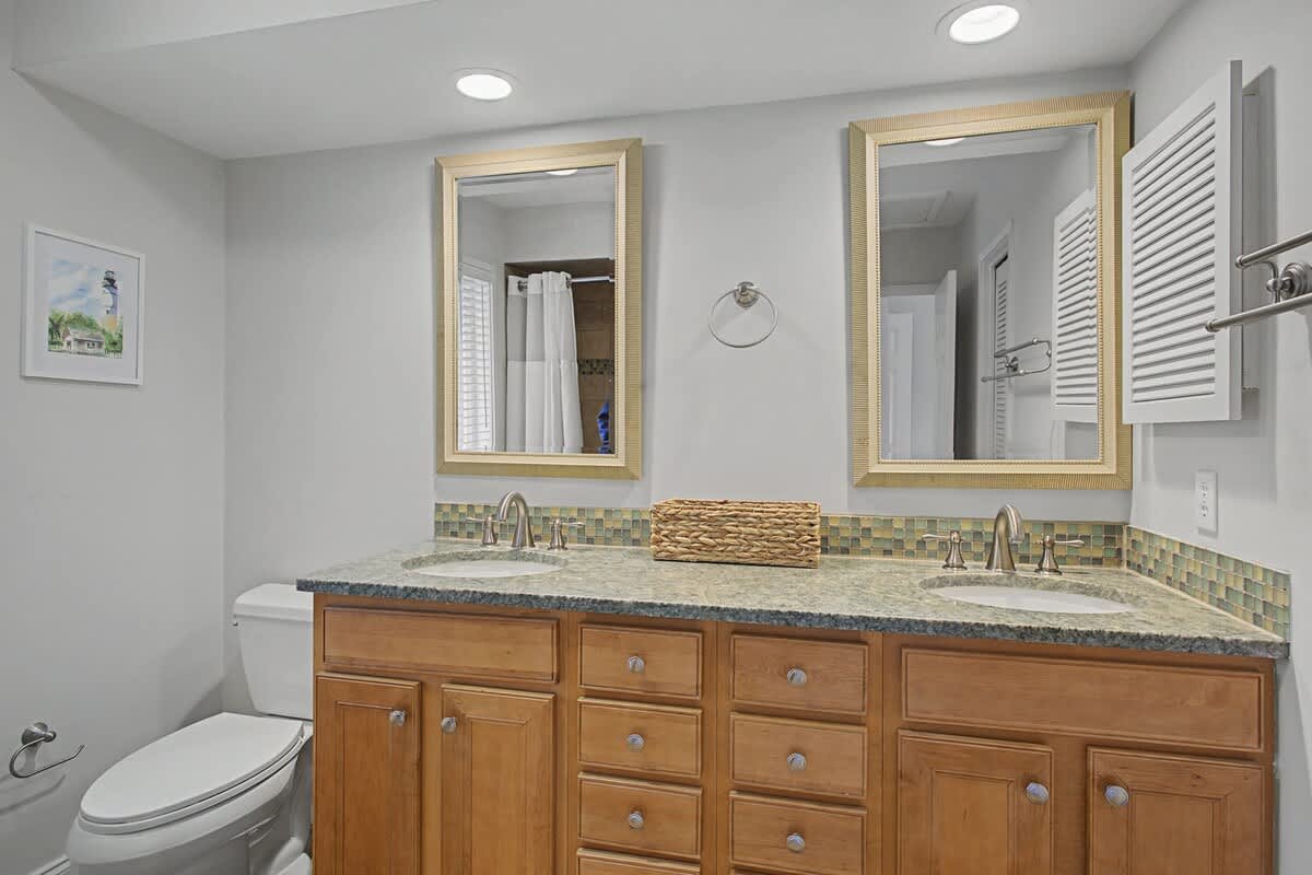 Your spacious dual-sink bathroom features warm wood vanity, granite countertops, and elegant gold-framed mirrors—perfect for your morning routine.