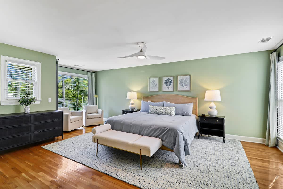 Unwind in your serene bedroom sanctuary with calming sage walls, plush bedding, and peaceful garden views through large windows.