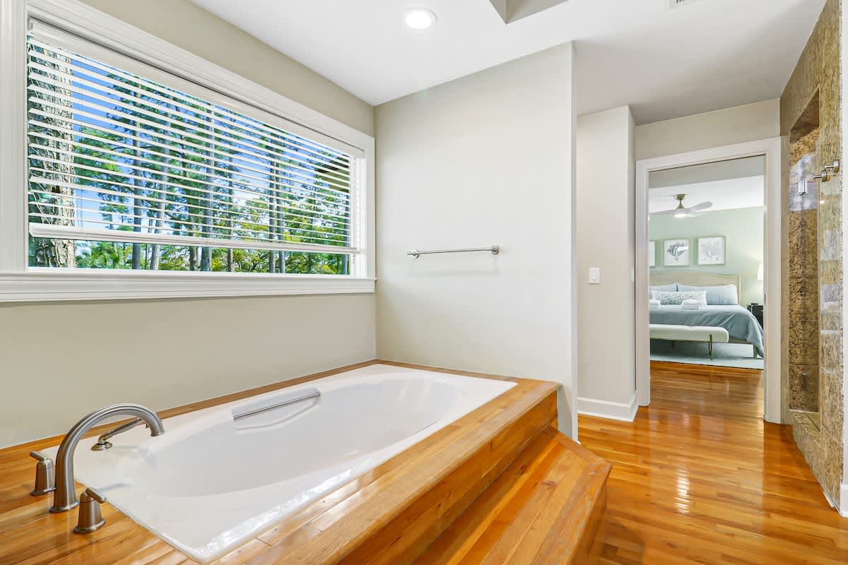 Unwind in your private spa-like bathroom featuring a deep soaking tub, polished hardwood floors, and leafy garden views.