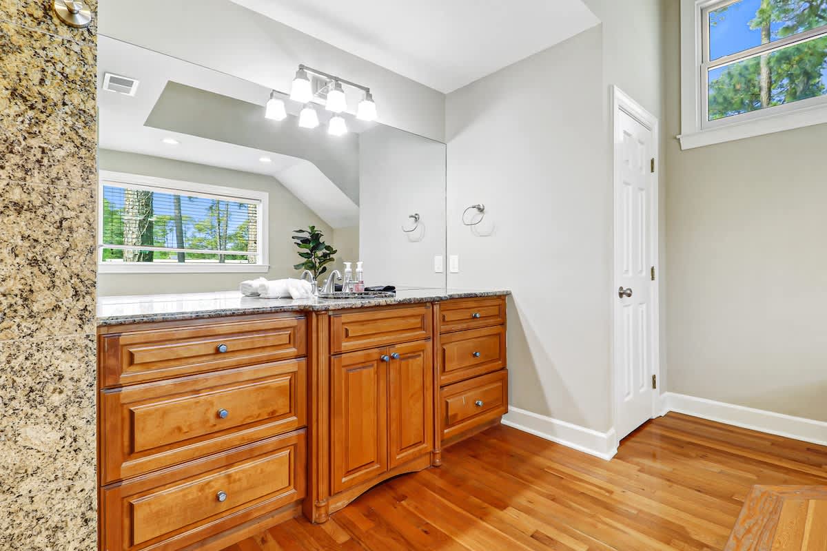 Refresh in this elegant bathroom featuring granite countertops, warm wood cabinetry, and bright natural light streaming through the windows.