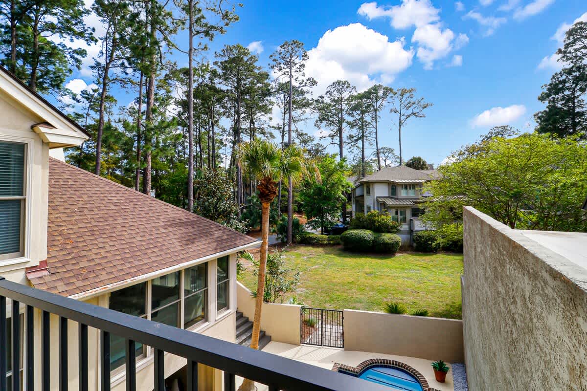 A peaceful residential property nestled among tall pines with well-maintained grounds and neighboring homes visible in the distance.