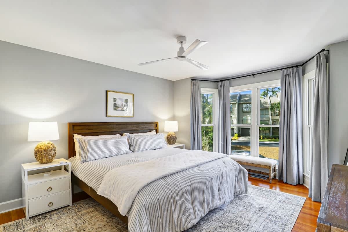 Drift off to sleep in your serene bedroom with crisp linens, gentle ceiling fan, and peaceful neighborhood views through floor-to-ceiling windows.