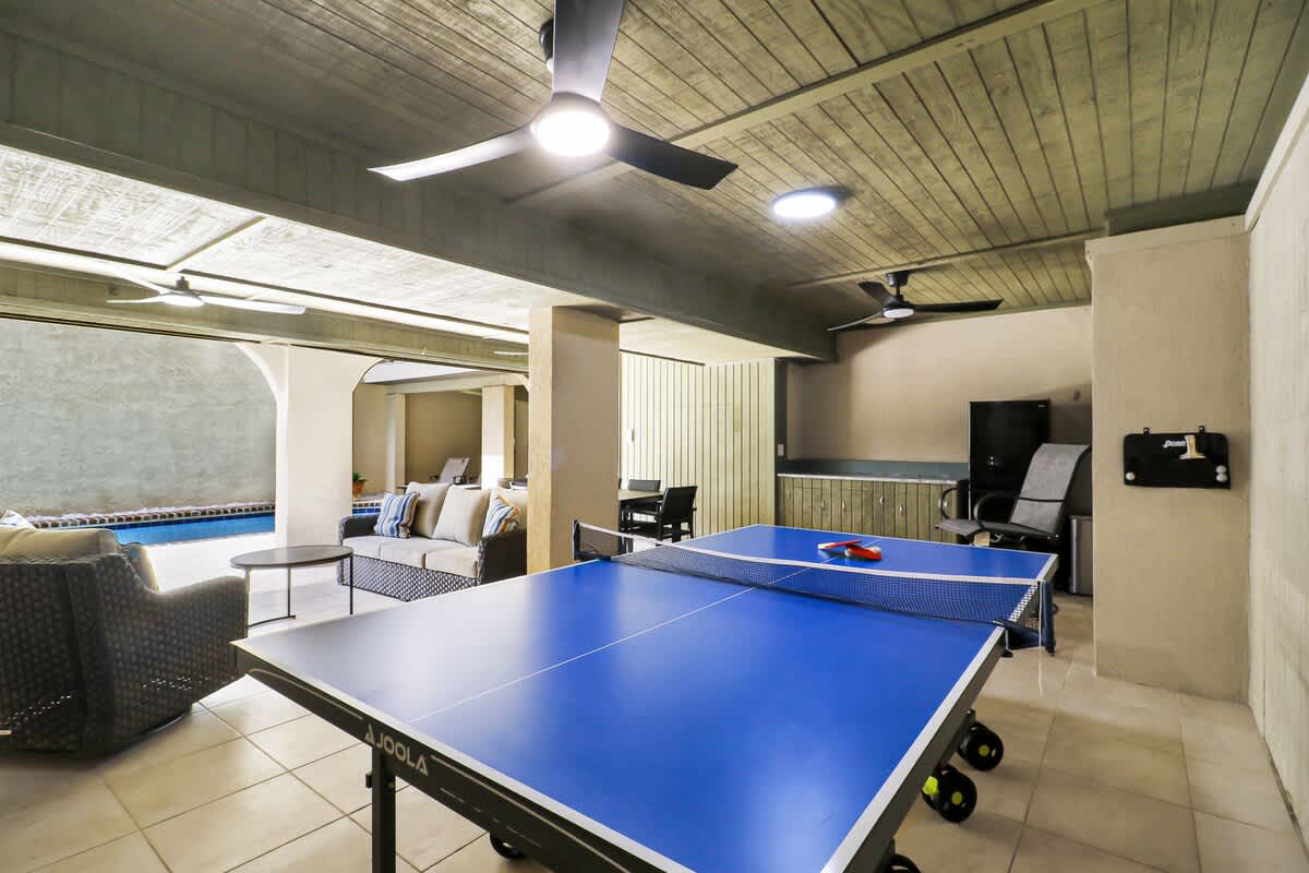 Covered ground-level entertainment space featuring a ping pong table, ample seating, and easy access to the pool - ideal for indoor-outdoor recreation.