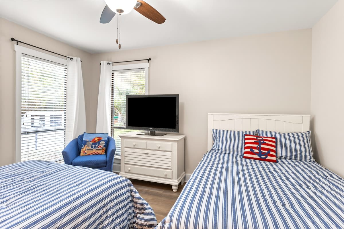 Relax in your cheerful double bedroom with nautical-striped bedding, flat-screen TV, and cozy reading chair by bright windows.