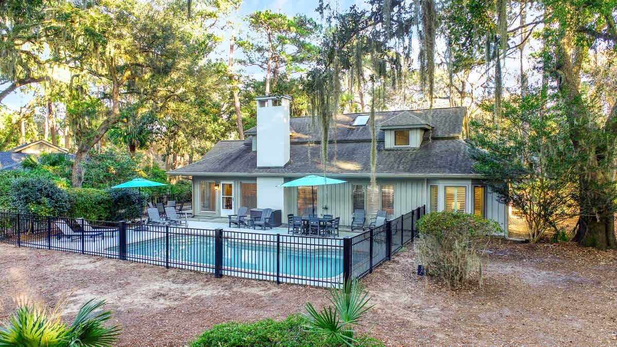Charming vacation home nestled among mature trees with private pool and spacious outdoor entertaining area surrounded by lush natural landscape.