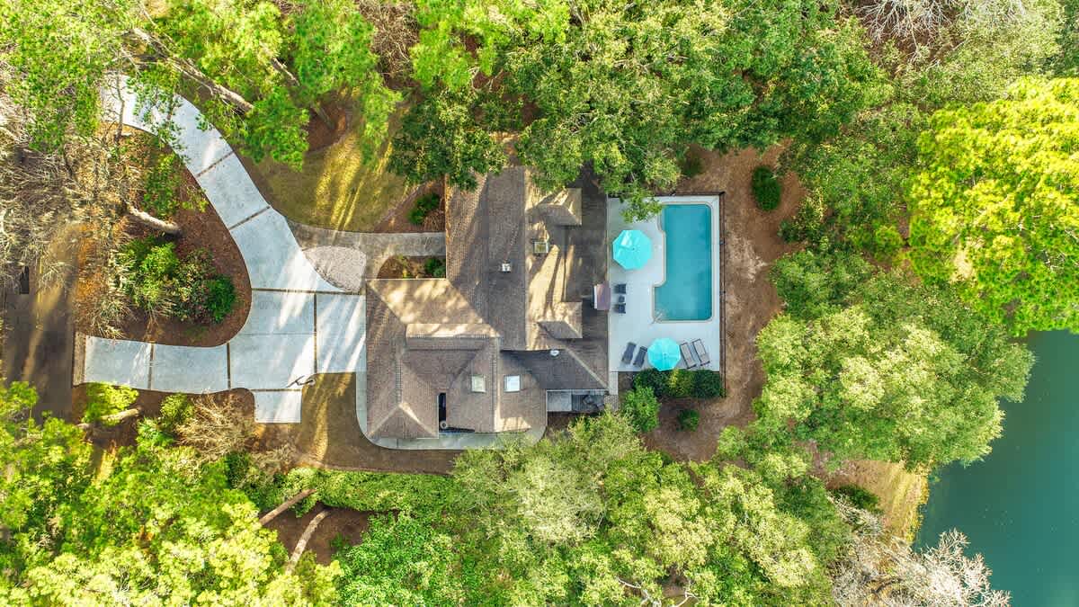 Aerial view of a tranquil lakeside property featuring a swimming pool, spacious outdoor areas, and winding driveway surrounded by lush greenery.