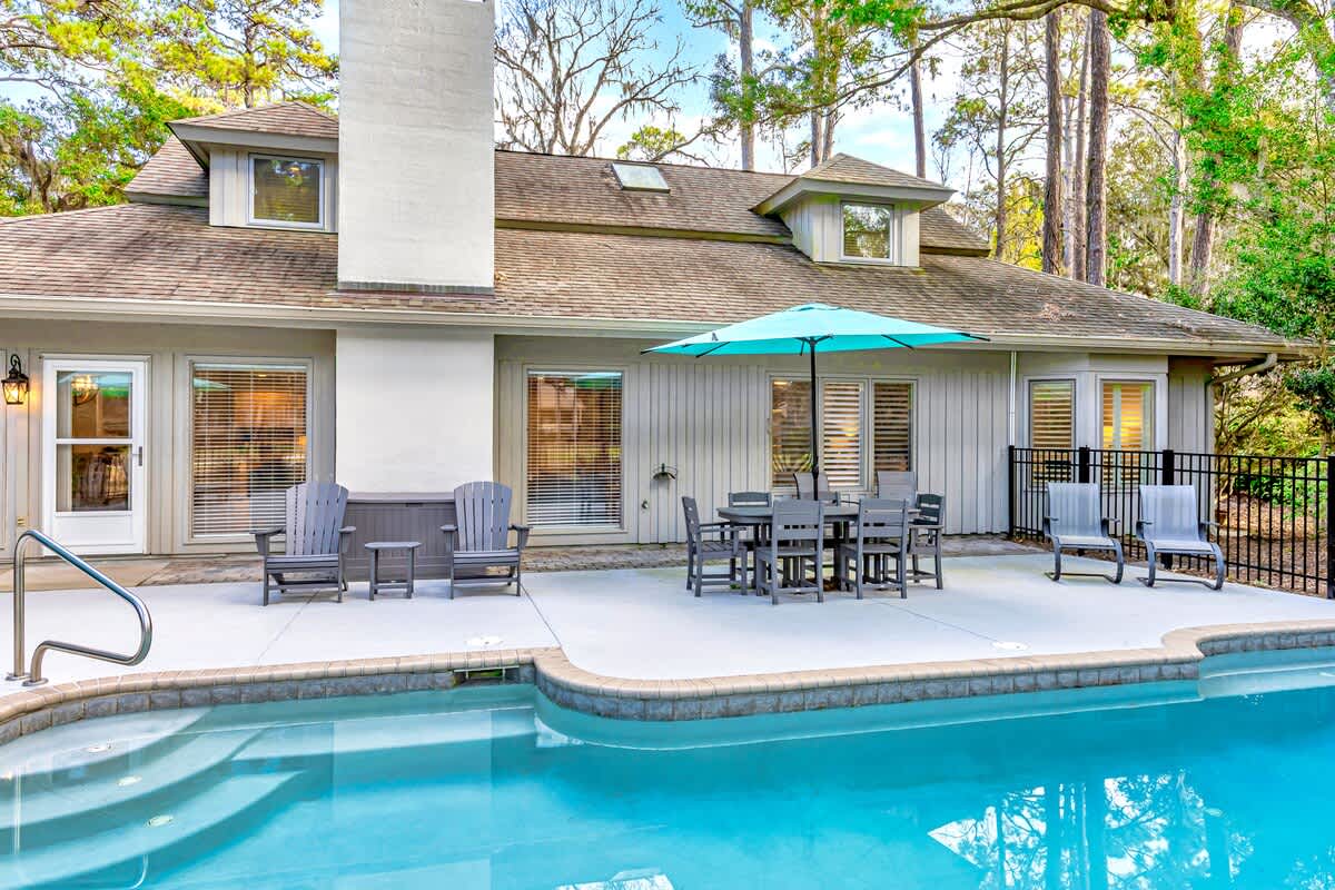 Your private oasis awaits with a sparkling pool, spacious patio dining, and comfortable loungers under swaying trees.