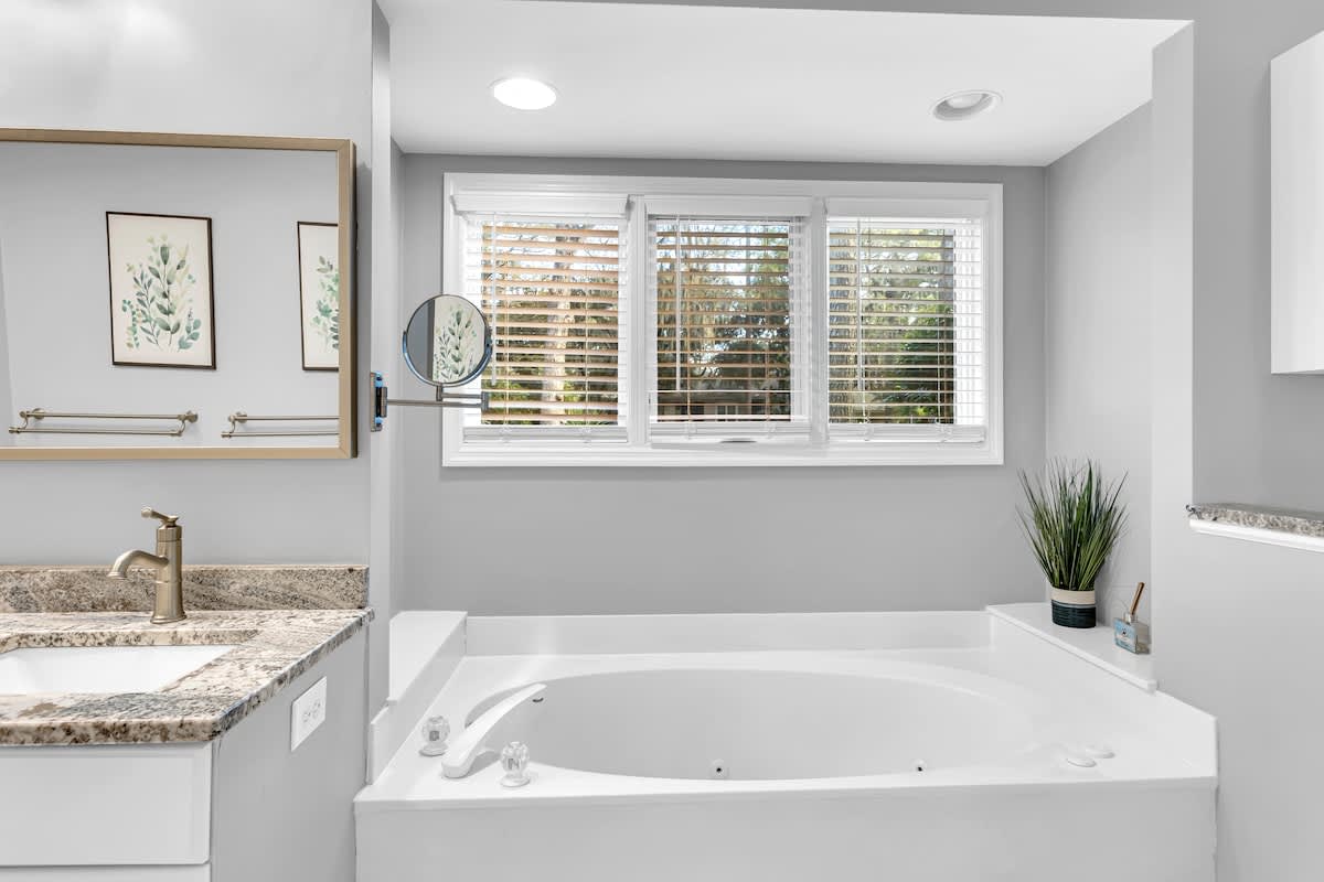 Unwind in your spa-like bathroom featuring a deep soaking tub, granite vanity, and natural light from plantation shutters.