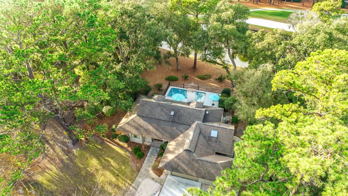 Aerial view of a charming property nestled among mature trees, featuring a sparkling swimming pool and peaceful residential setting.
