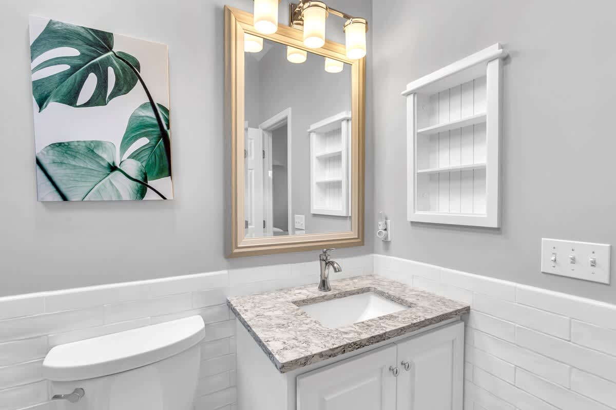 Refresh in your beautifully appointed bathroom featuring elegant marble countertops, bright vanity lighting, and tropical artwork that creates a serene spa-like atmosphere.