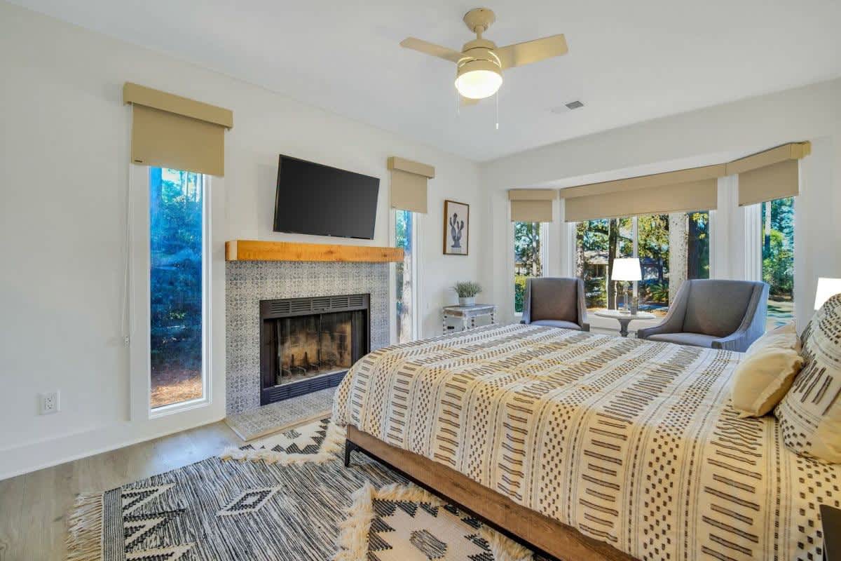 Unwind in your elegant bedroom featuring a cozy fireplace, flat-screen TV, and panoramic windows overlooking lush gardens.